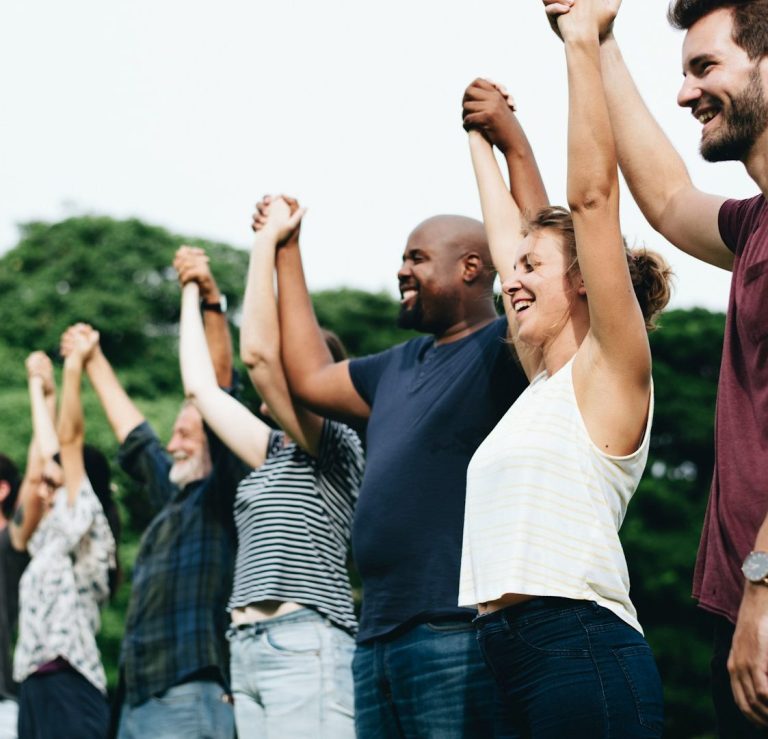 Gruppe von Menschen, die ihre Arme heben, lächeln und zusammen Freude zeigen.